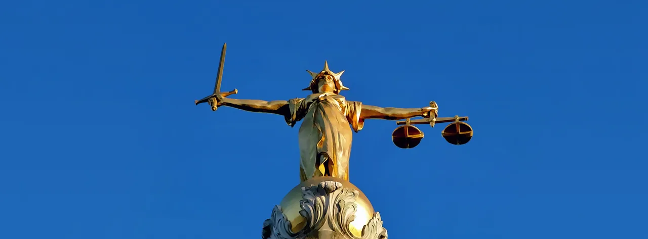Una estatua de la Dama de la Justicia, una personificación de la justicia, a menudo representada con una balanza y una espada, simbolizando la equidad y la imparcialidad de la ley, un concepto desafiado por el sesgo algorítmico.